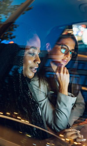 Young multiracial business woman working together while traveling by a car during a night. They are using laptop and preparing for meeting. Transportation in corporate business concept. Copy space.