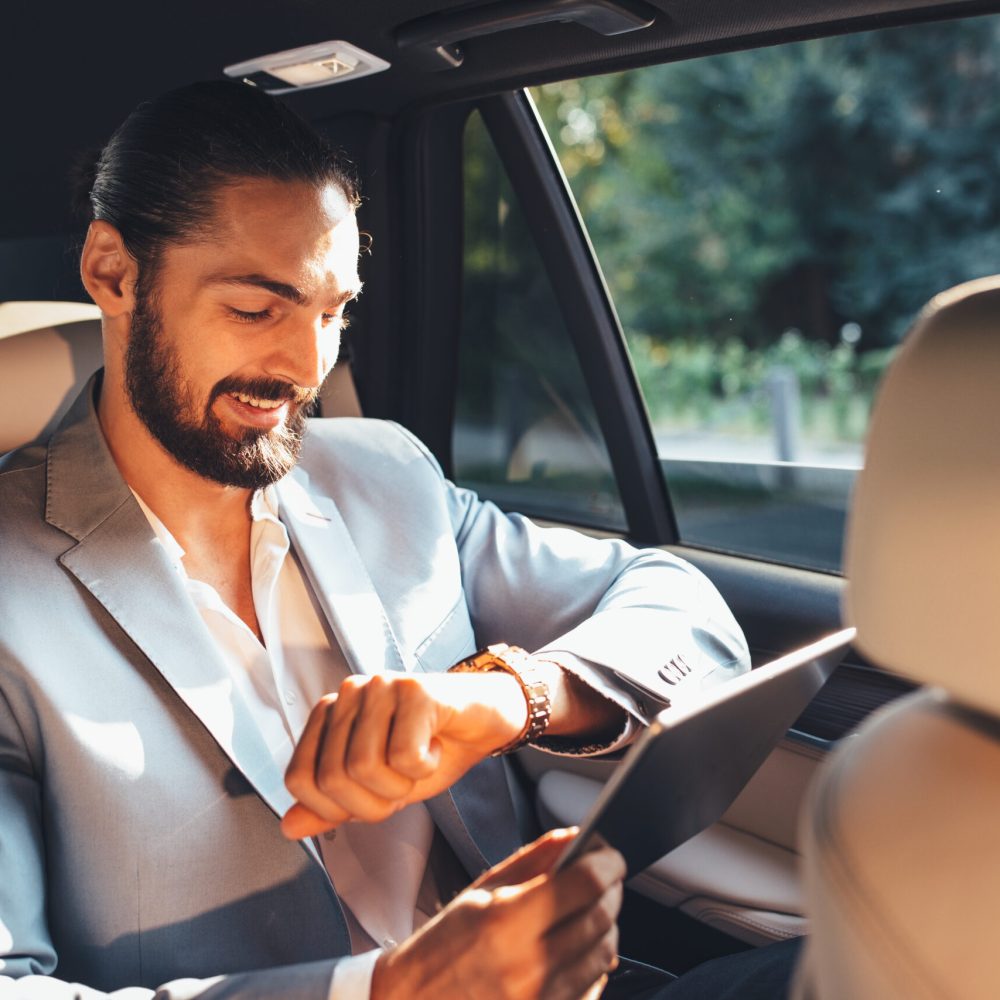 Businessman looking at the watch on the back of the limousine